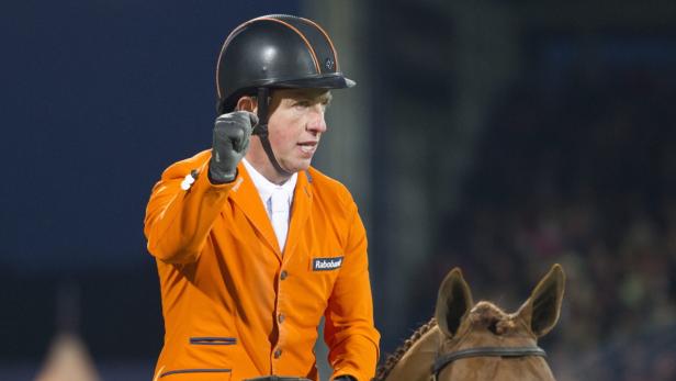 Ein Reiter in oranger Jacke und Helm jubelt auf seinem Pferd.