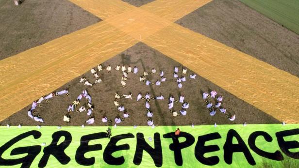 Luftaufnahme einer Greenpeace-Demonstration mit gelbem Kreuz und Aktivisten, die „Act Now“ bilden.