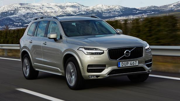 Ein silberner Volvo XC90 fährt auf einer Straße mit schneebedeckten Bergen im Hintergrund.
