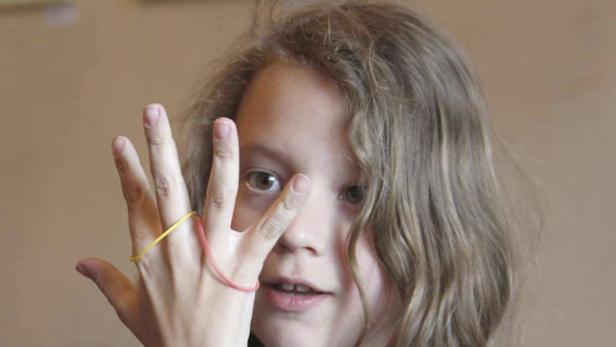 Ein Mädchen hält ihre Hand mit Gummibändern vor ihr Gesicht.