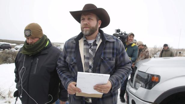 Ein Mann mit Cowboyhut hält ein Blatt Papier in der Hand, umgeben von anderen Personen im Freien.