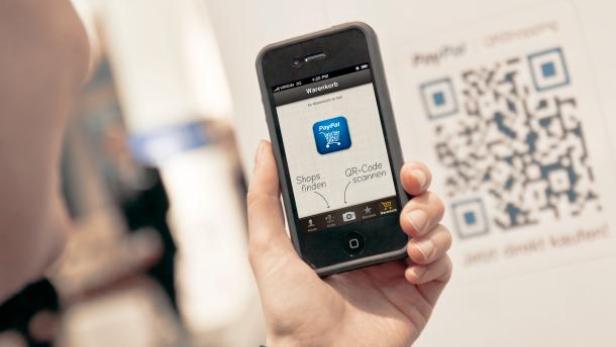 Eine Person hält ein Smartphone mit der PayPal-App vor einen QR-Code.