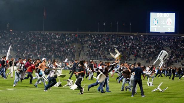Nach dem Fußballspiel stürmen Fans den Platz und werfen mit Stühlen.