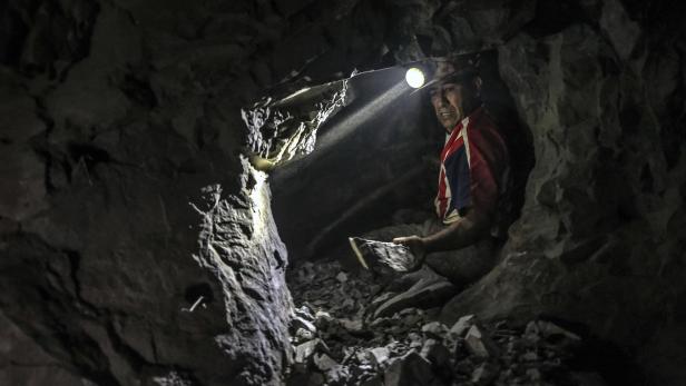 Ein Bergmann sitzt in einem dunklen Stollen mit einer Lampe am Helm.