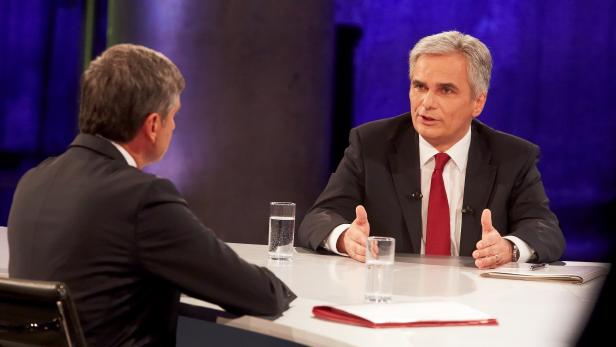 Zwei Männer sitzen an einem Tisch und diskutieren vor blauem Hintergrund.