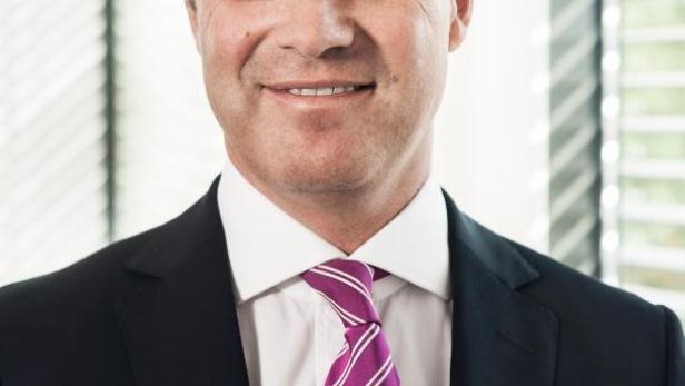 Ein Mann im Anzug mit einer gestreiften, pinkfarbenen Krawatte lächelt in die Kamera.