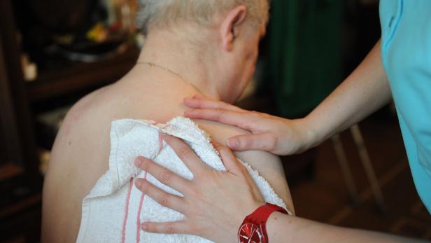 Eine Pflegekraft wäscht den Rücken einer älteren Person mit einem Waschlappen.
