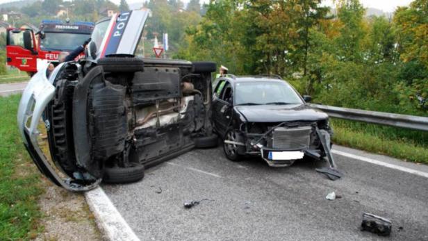 Zwei beschädigte Autos nach einem Unfall, eines davon ein Polizeiwagen, stehen auf der Straße.