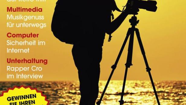 Ein Fotograf mit Rucksack und Stativ fotografiert am Meer bei Sonnenuntergang.