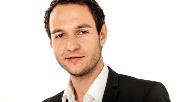 Ein junger Mann im Anzug lächelt in die Kamera.