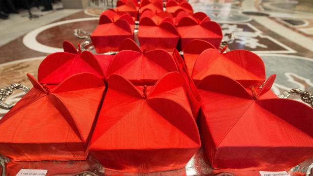 Mehrere rote Kardinalshüte liegen auf einem Tisch.