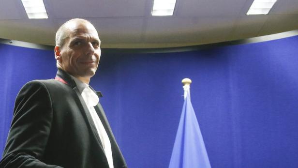 Ein Mann in Anzug und Fliege steht vor einer blauen Wand und einer Flagge.