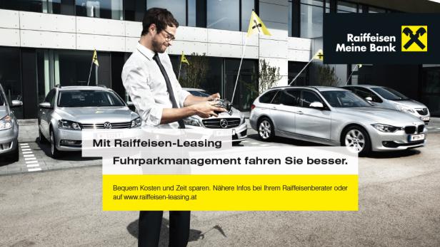 Ein Mann steuert ein Modellauto mit einer Fernbedienung vor einer Reihe von Autos mit Raiffeisen-Flaggen.