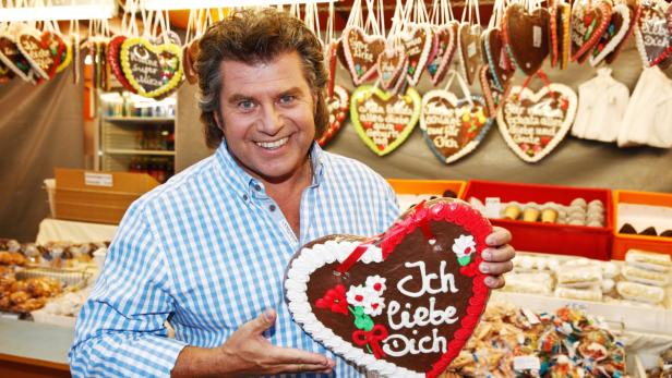 Ein lächelnder Mann hält ein Lebkuchenherz mit der Aufschrift „Ich liebe Dich“.