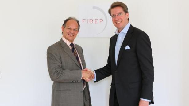 Zwei Männer in Anzügen schütteln sich vor einem FIBEP-Logo die Hände.