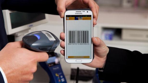 Ein Mann hält ein Smartphone mit einem Barcode vor einen Scanner.