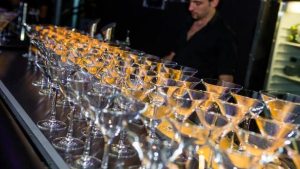 Ein Barkeeper steht hinter einer langen Reihe von Martini-Gläsern.