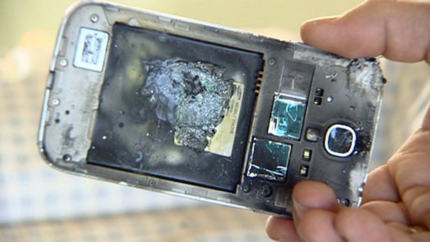 Ein beschädigtes Smartphone mit aufgeblähtem Akku wird von einer Hand gehalten.