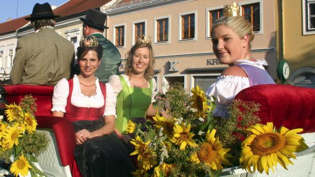 Drei junge Frauen mit Dirndl und Krönchen sitzen in einer Kutsche, geschmückt mit Sonnenblumen.