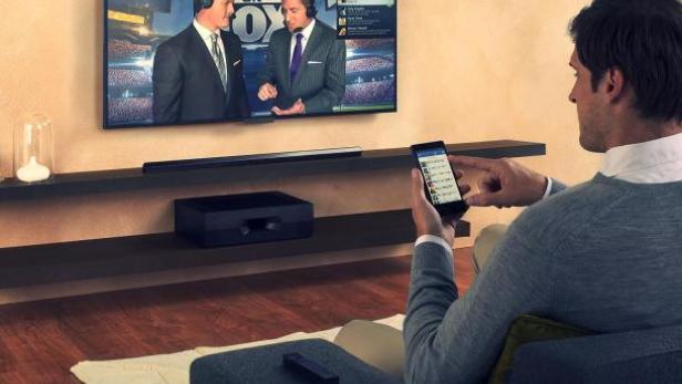 Ein Mann sitzt vor dem Fernseher und benutzt sein Smartphone.