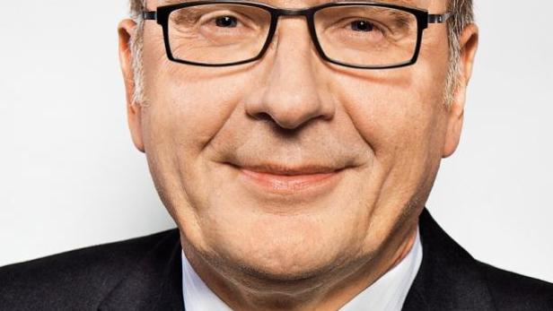 Ein Mann mit Brille, Anzug und Krawatte lächelt in die Kamera.