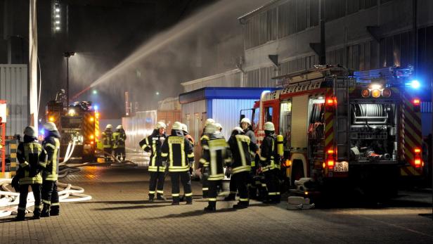 Feuerwehrleute stehen bei Nacht vor einem Feuerwehrwagen und löschen ein Feuer.