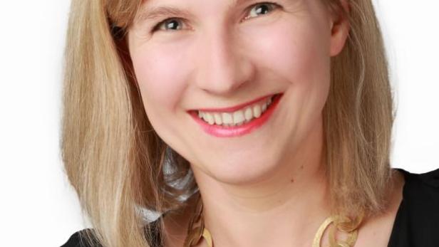 Eine lächelnde Frau mit blonden Haaren und einer goldenen Halskette.