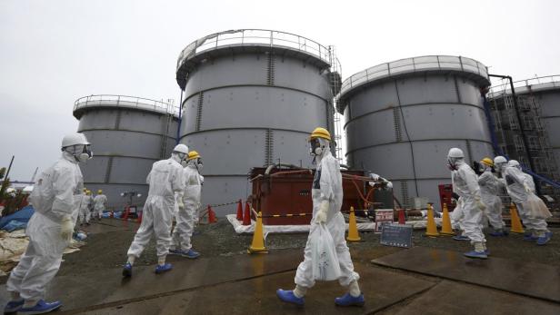 Arbeiter in Schutzanzügen inspizieren große Tanks in Fukushima.