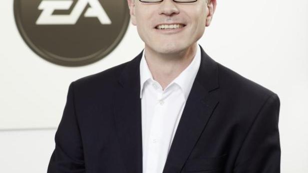 Ein Mann mit Brille und Anzug vor dem EA-Logo lächelt in die Kamera.