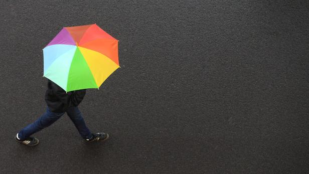 Eine Person geht mit einem Regenbogen-Regenschirm auf einer dunklen Straße.