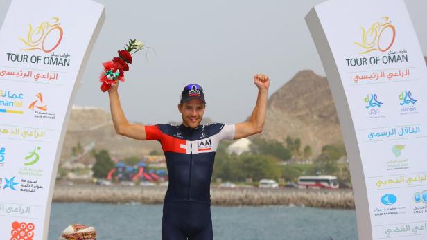 Ein Radrennfahrer feiert seinen Sieg bei der Tour of Oman mit einem Blumenstrauß.