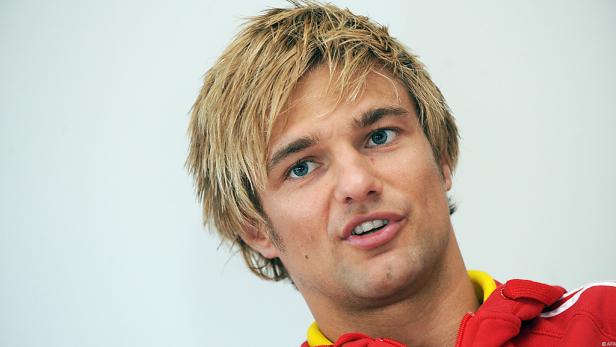 Ein Mann mit blonden Haaren und blauen Augen schaut in die Kamera.