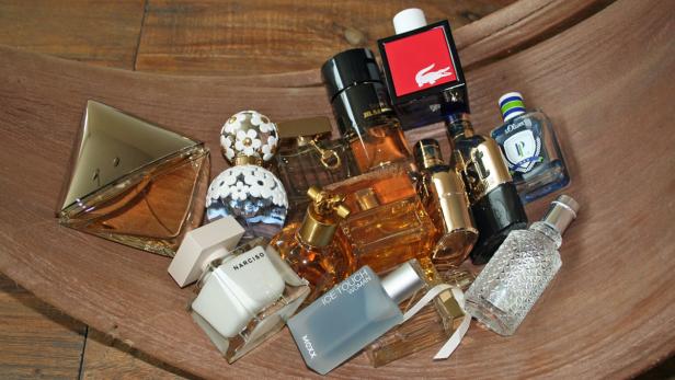Verschiedene Parfümflaschen unterschiedlicher Marken und Formen liegen in einer Holzschale.