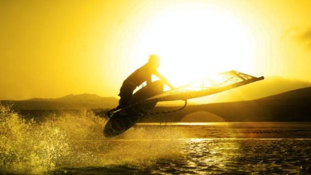Ein Windsurfer springt bei Sonnenuntergang über das Wasser.
