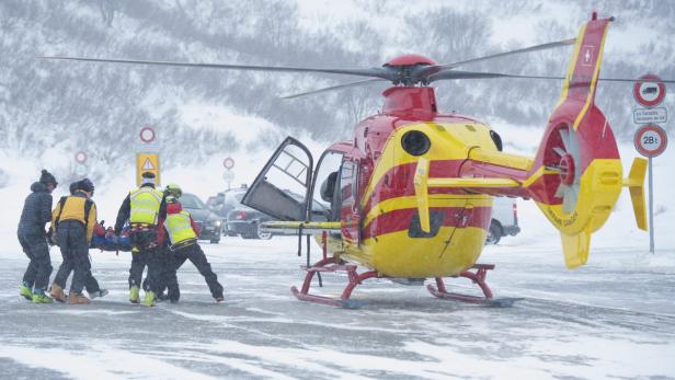 Rettungskräfte tragen eine Person auf einer Trage zu einem gelb-roten Rettungshubschrauber.