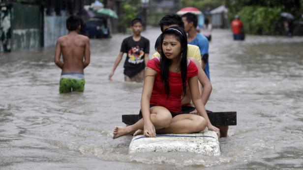 Eine junge Frau sitzt auf einem improvisierten Floß, während andere durch das Hochwasser waten.