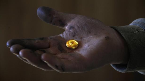 Eine schmutzige Hand hält ein Nugget aus Gold.