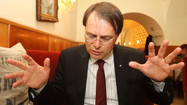 Ein Mann mit Brille und Anzug gestikuliert mit beiden Händen.