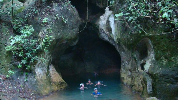 Eine Gruppe von Menschen schwimmt in einer Höhle mit türkisfarbenem Wasser.
