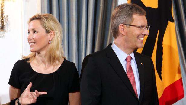Eine Frau und ein Mann stehen lächelnd vor einer Deutschlandflagge.
