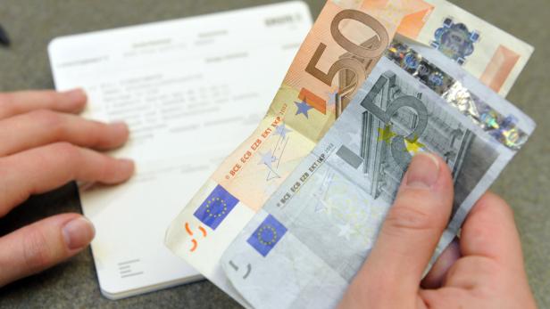 Eine Hand hält einen Fünfziger und einen Fünf-Euro-Schein über einem Dokument.