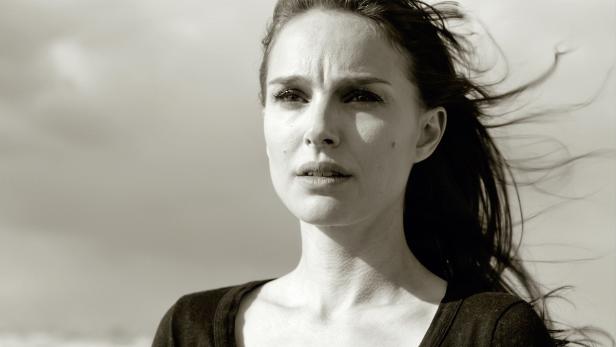 Schwarzweißporträt von Natalie Portman mit wehendem Haar vor einem bewölkten Himmel.