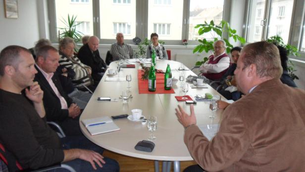 Eine Gruppe von Menschen sitzt an einem ovalen Tisch in einem Konferenzraum.