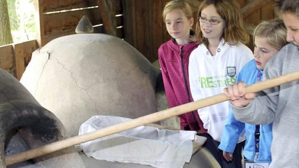 Eine Gruppe Kinder backt Brot in einem traditionellen Steinofen.