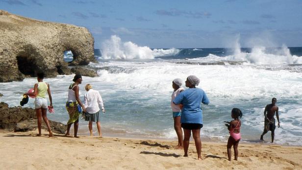 Eine Gruppe von Menschen genießt den Tag an einem Sandstrand mit starkem Wellengang.