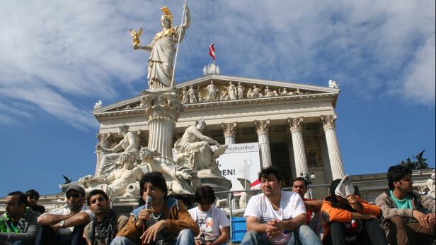Eine Gruppe von Menschen sitzt vor dem österreichischen Parlament in Wien.