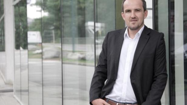 Ein Mann in Jeans und Sakko steht vor einem modernen Gebäude.