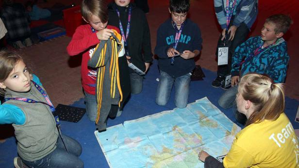 Eine Gruppe Kinder kniet um eine Weltkarte auf dem Boden.