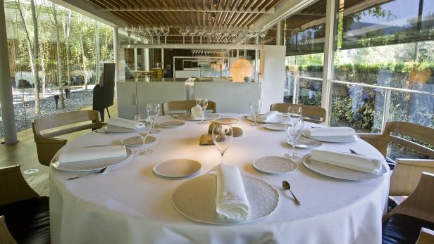 Ein runder Tisch mit weißer Tischdecke ist für ein formelles Abendessen in einem hellen Raum gedeckt.