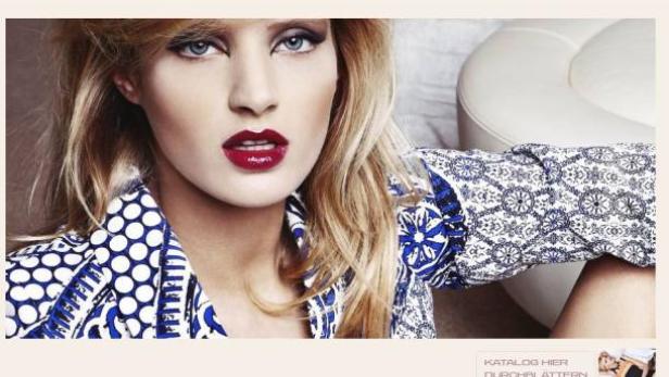 Eine blonde Frau mit rotem Lippenstift trägt eine blau-weiß gemusterte Bluse.